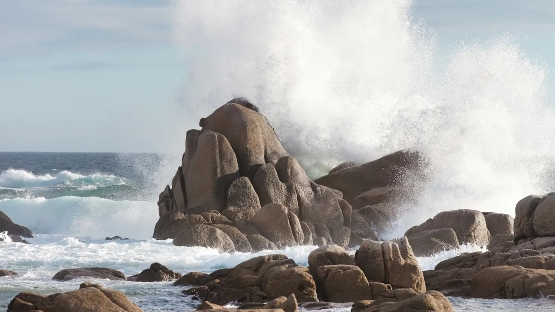 Waves break on rocks on a shore.